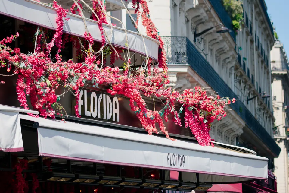 Paris café front with white awnings and cascading pink blossom draped along the balcony above