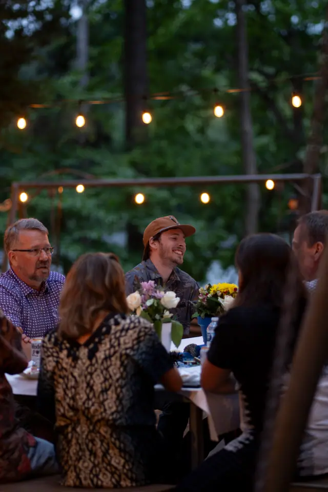 Guests seated at a long table under warm string lights at an outdoor evening reception