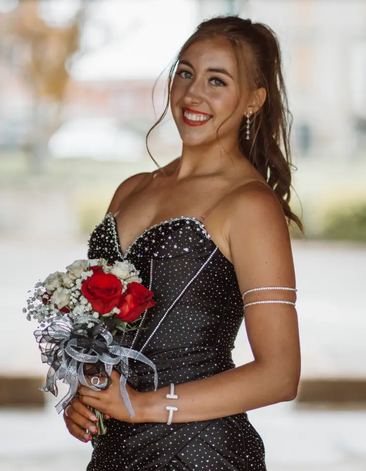 Smiling young woman in a black sequined strapless prom dress holding a bouquet of red and white roses